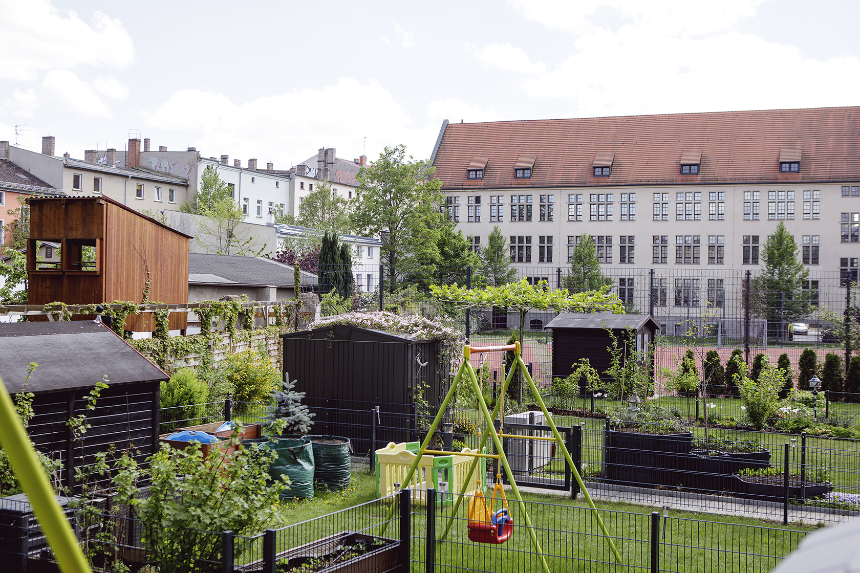 Abgebildet sind kleine Gärten mit Schuppen, Pflanzen und einer Schaukel. Im Hintergrund stehen Wohnhäuser.