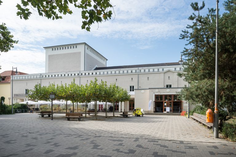 Zu sehen ist das ehemalige Theater Karlshorst, fotografiert vom Johannes-Fest-Platz. Der Himmel ist blau.