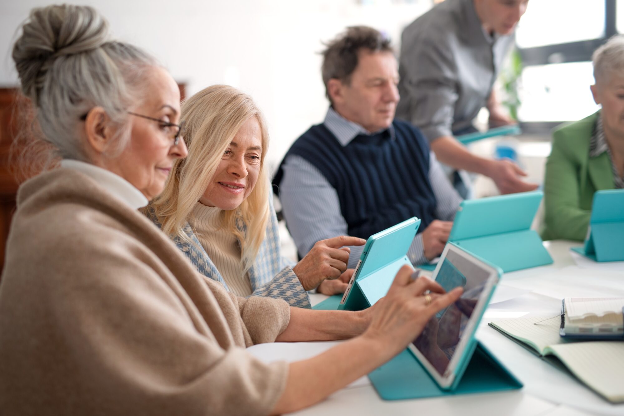 Abgebildet sind mehrere Menschen nebeneinander am Tisch sitzend mit einem Tablet.