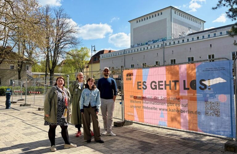Das Team der Stiftung Stadtkultur steht vor dem KAHO in Karlshorst. Daneben ist ein buntes Banner zum Sanierungsstart des KAHO zu sehen.
