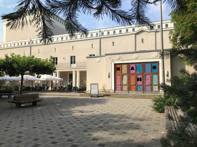 Fotografie des ehemaligen Theaters Karlshorst vom Johannes-Fest-Platz. Sonniger Tag und blauer Himmel.